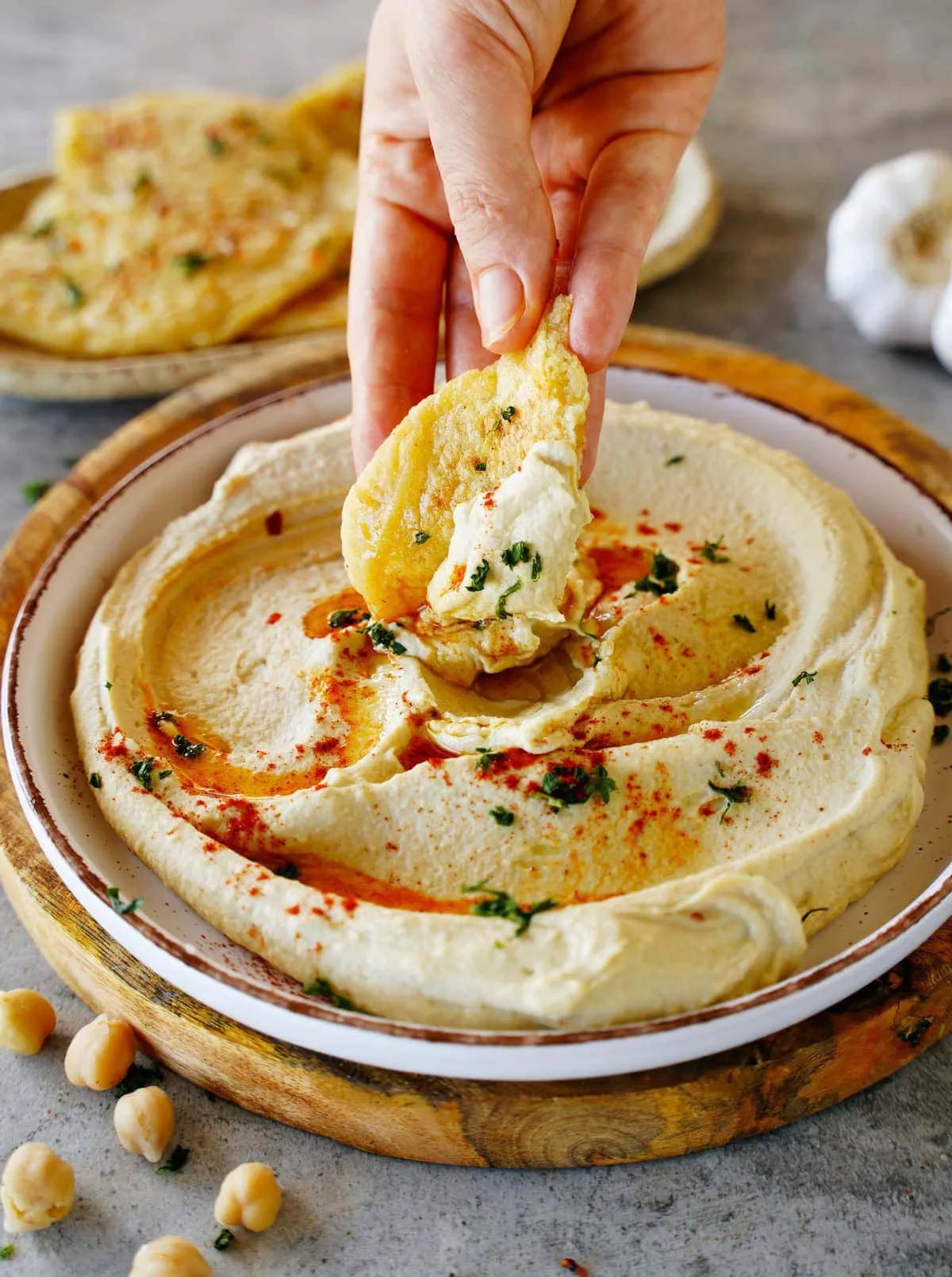 Eine Hand dippt ein Stück Fladenbrot in selbstgemachten, cremigen Hummus, ein klassischer Genuss