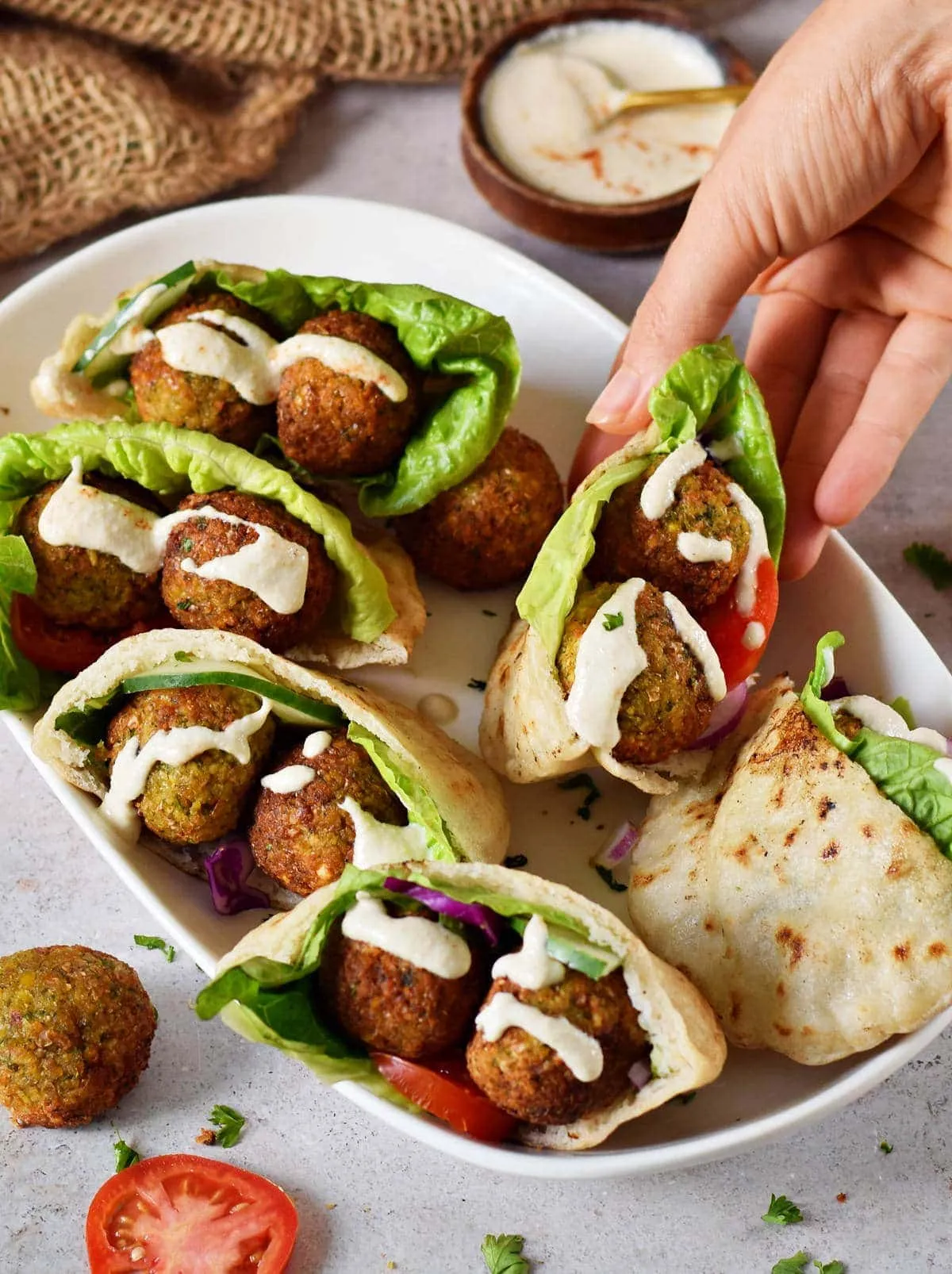Eine Hand greift eine glutenfreie Pita, gefüllt mit knusprigen Falafeln, Hummus und Salat, ideal für ein schnelles veganes Mittagessen.