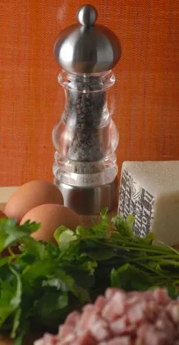 Eine Hand mahlt frischen schwarzen Pfeffer mit einer Holzmühle über eine Portion Spaghetti Carbonara, bereit zum Servieren.