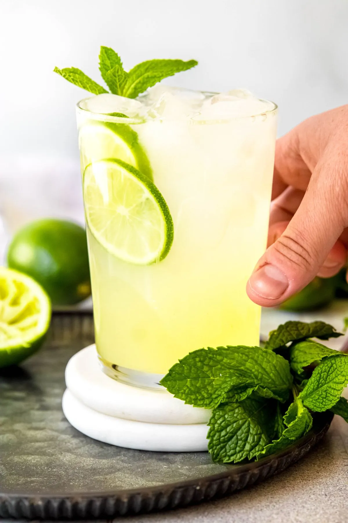 Eine Hand nimmt ein Glas selbstgemachten Cool Lime Refresher von einem Serviertablett.