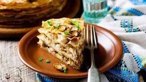 Eine herzhafte Pfannkuchentorte auf einem Teller, mit Kräutern garniert.