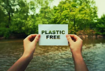 Eine junge Frau hält ein Schild mit der Aufschrift &quot;Plastic Free&quot; und lächelt