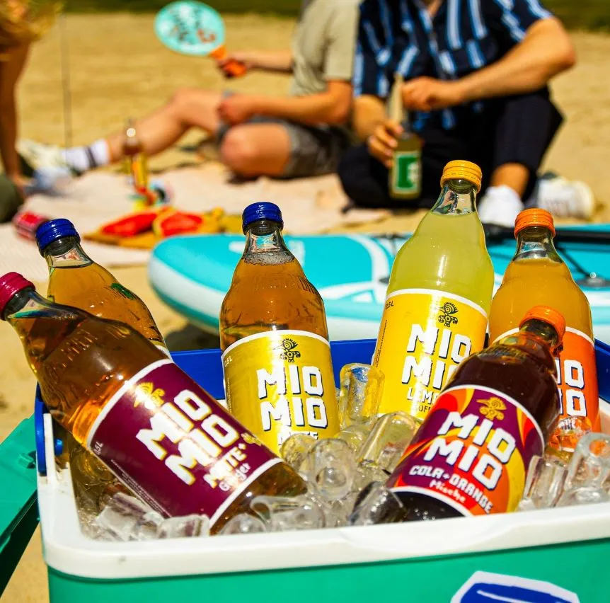 Eine Kühlbox voller Mio Mio Getränke am Strand, ideal für sommerliche Erfrischung und entspannte Momente