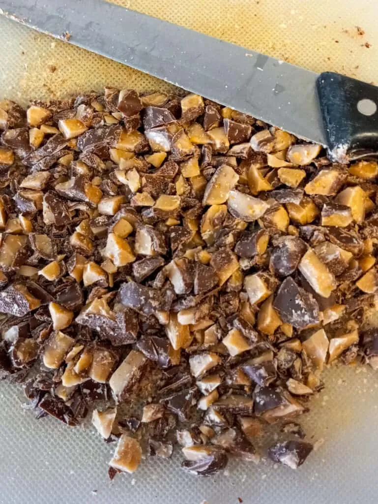 Eine Nahaufnahme von gehackten Heath Toffee-Riegeln auf einem Schneidebrett, bereit zur Verwendung in der Tiramisu Kuchenmischung.
