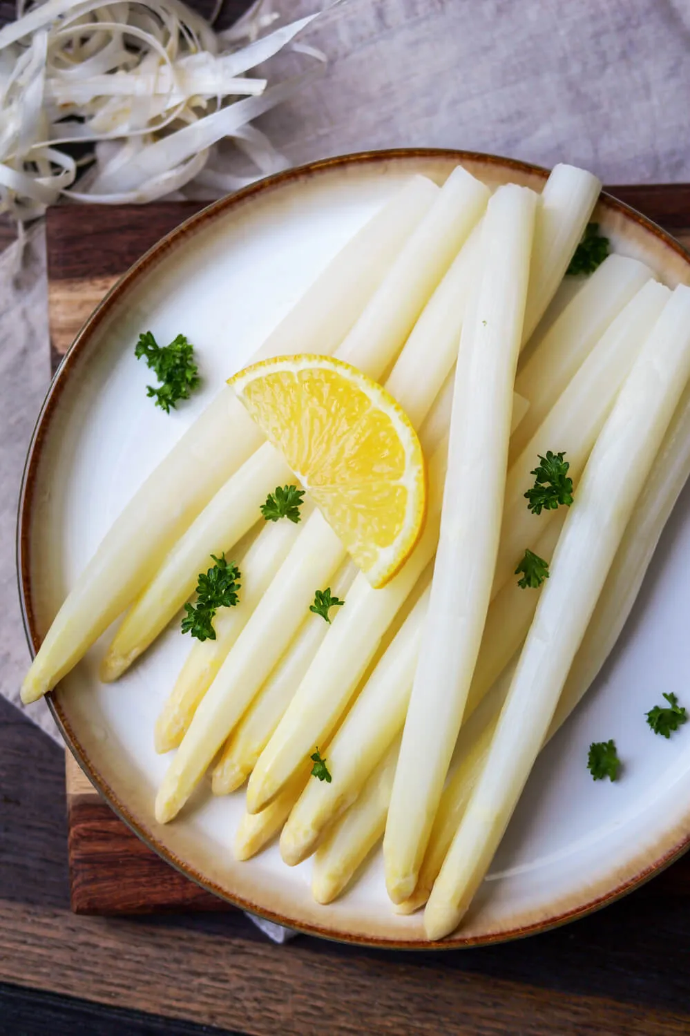 Eine Nahaufnahme von perfekt gegartem weißen Spargel, garniert mit Zitrone und frischer Petersilie, präsentiert als einfaches Spargelrezept.