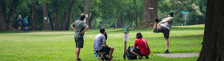 Eine Person, die eine Frisbeescheibe (Disc Golf) wirft, in einer dynamischen Bewegung auf einem Feld.