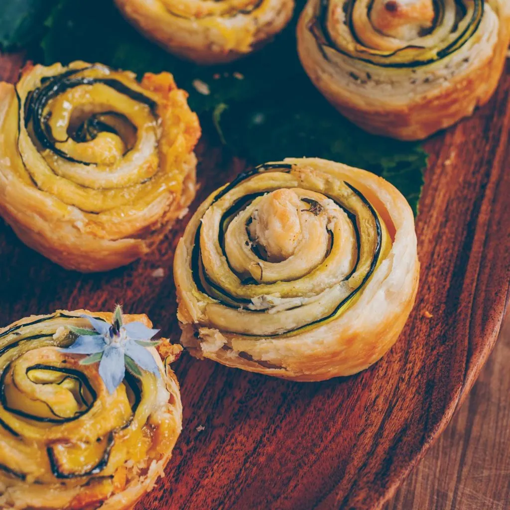 Eine Person rollt Zucchinischeiben und Blätterteig zu einer dekorativen Rose