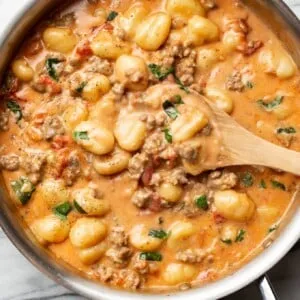 Eine Pfanne mit italienischer Wurst Gnocchi und einem Holzlöffel