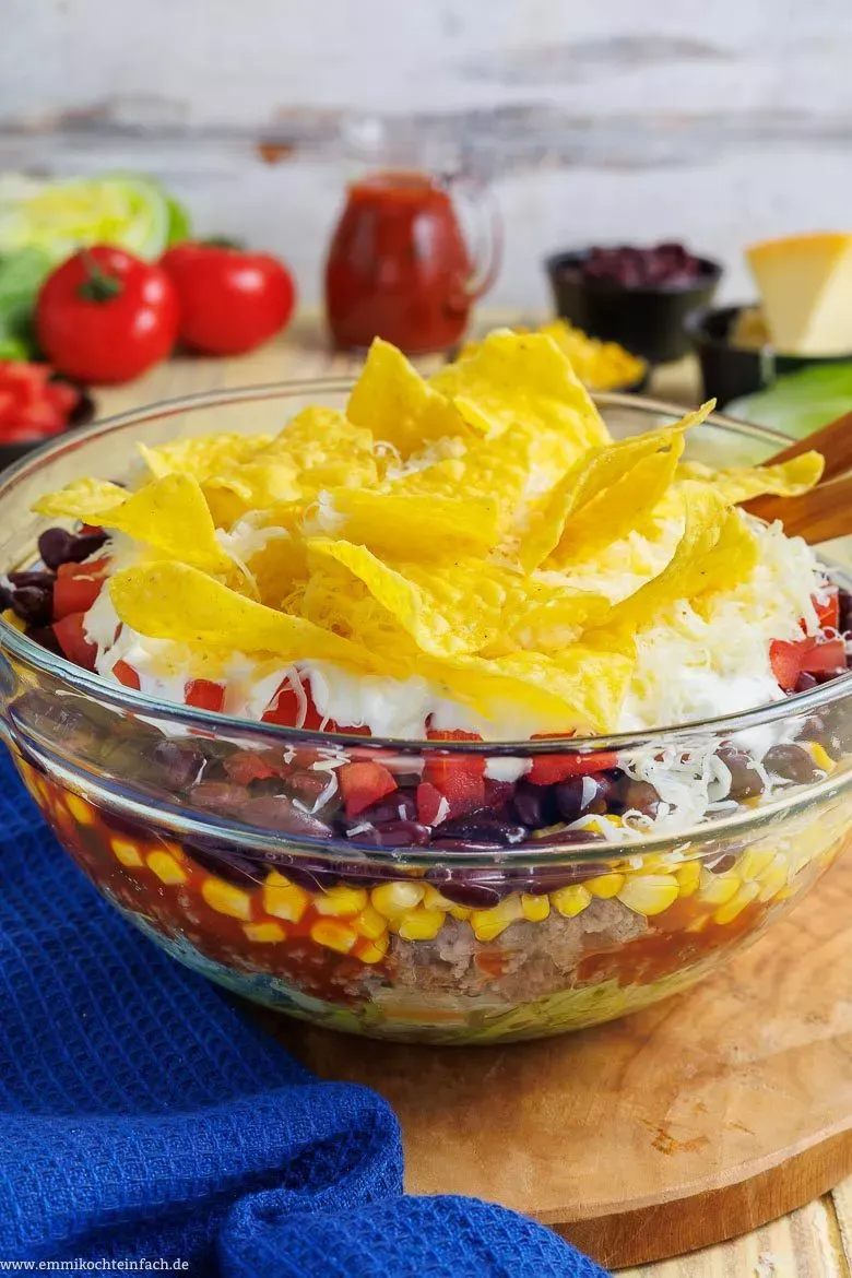 Eine Portion des cremigen und knackigen Taco Salats in einer Glasschüssel, garniert mit frischen Tortilla-Chips, bereit für den Genuss auf einer Party oder beim Grillabend.