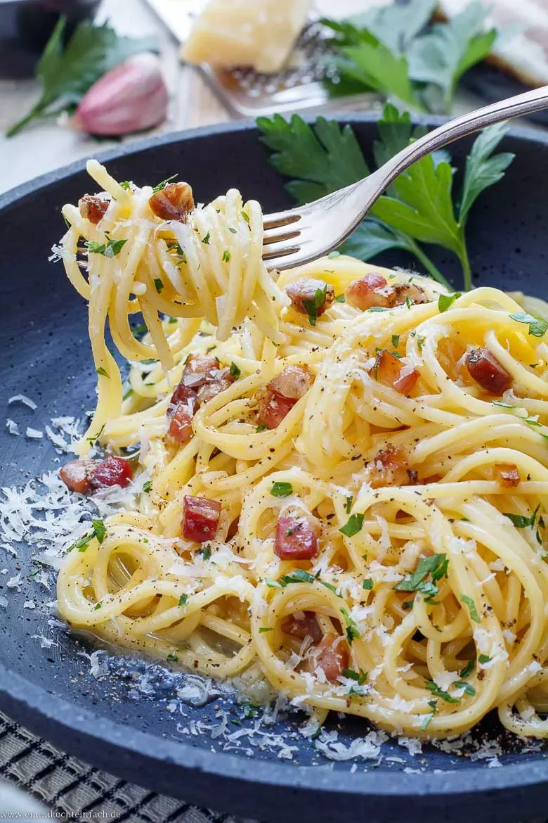 Eine Portion echter Spaghetti Carbonara mit perfekt emulgierter Soße, bereit zum Servieren und mit Parmesan garniert.