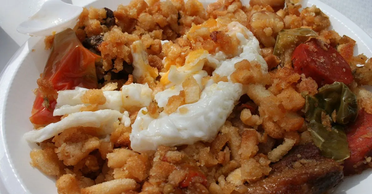 Eine Portion rustikaler Migas, ein Gericht aus zerbröseltem, gebratenem Brot, garniert mit Chorizo und einem Spiegelei, auf einem Holztisch