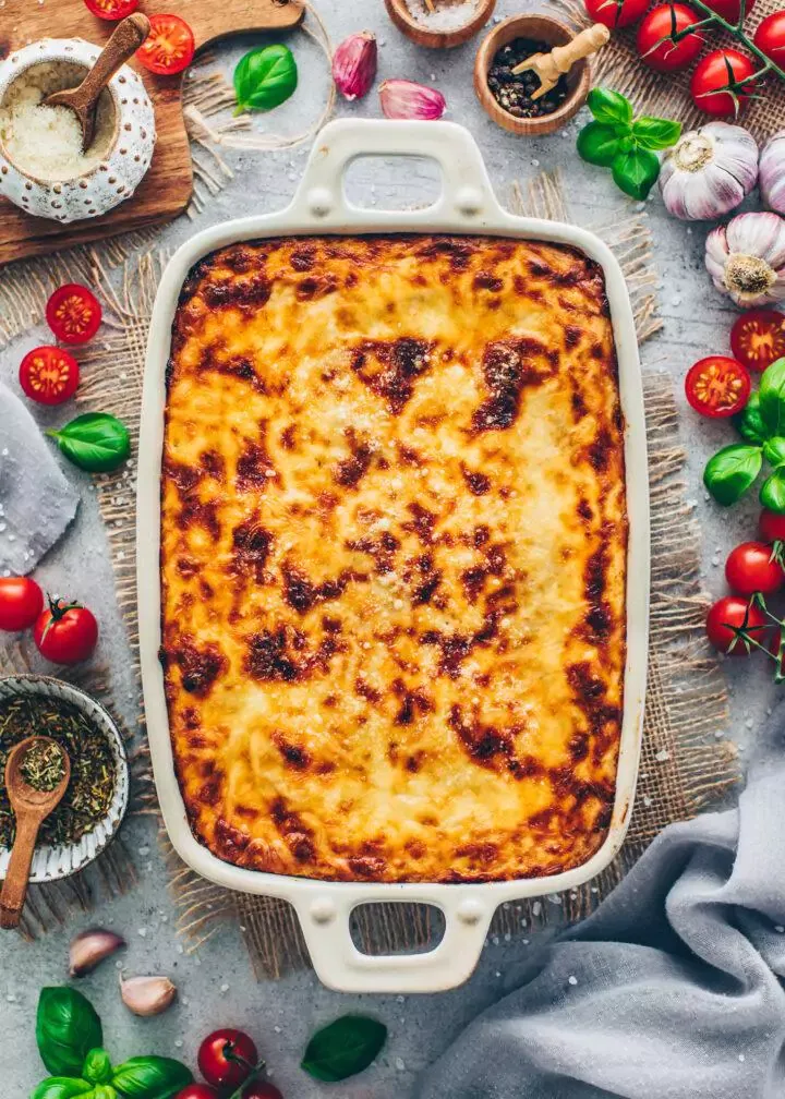 Eine reichhaltig gebackene vegane Lasagne, die aus der Auflaufform herausragt, mit einer köstlichen Käsekruste und frischem Basilikum.