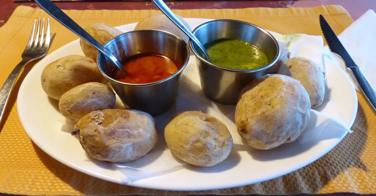 Eine Schale mit kleinen, runzligen Salzkartoffeln (Papas Arrugadas), daneben zwei Saucen: ein roter Mojo Picón und ein grüner Mojo Verde, auf einem rustikalen Holztisch