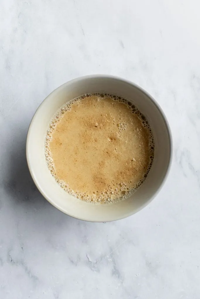 Eine Schale mit schaumiger Hefemischung aus warmer Milch, Hefe und Zucker, ein Zeichen für aktive Hefe.