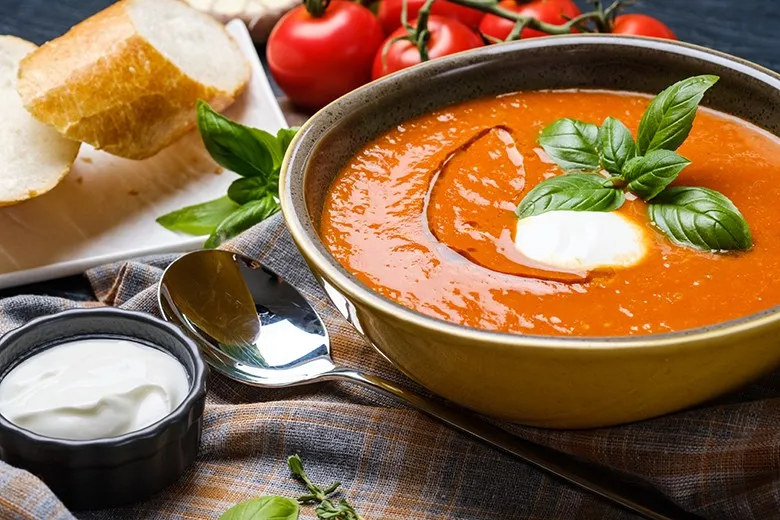 Eine Schüssel cremiger leichter Tomatensuppe, garniert mit Basilikum und einem Schuss Olivenöl, ein Beispiel für eine kalorienarme Vorspeise