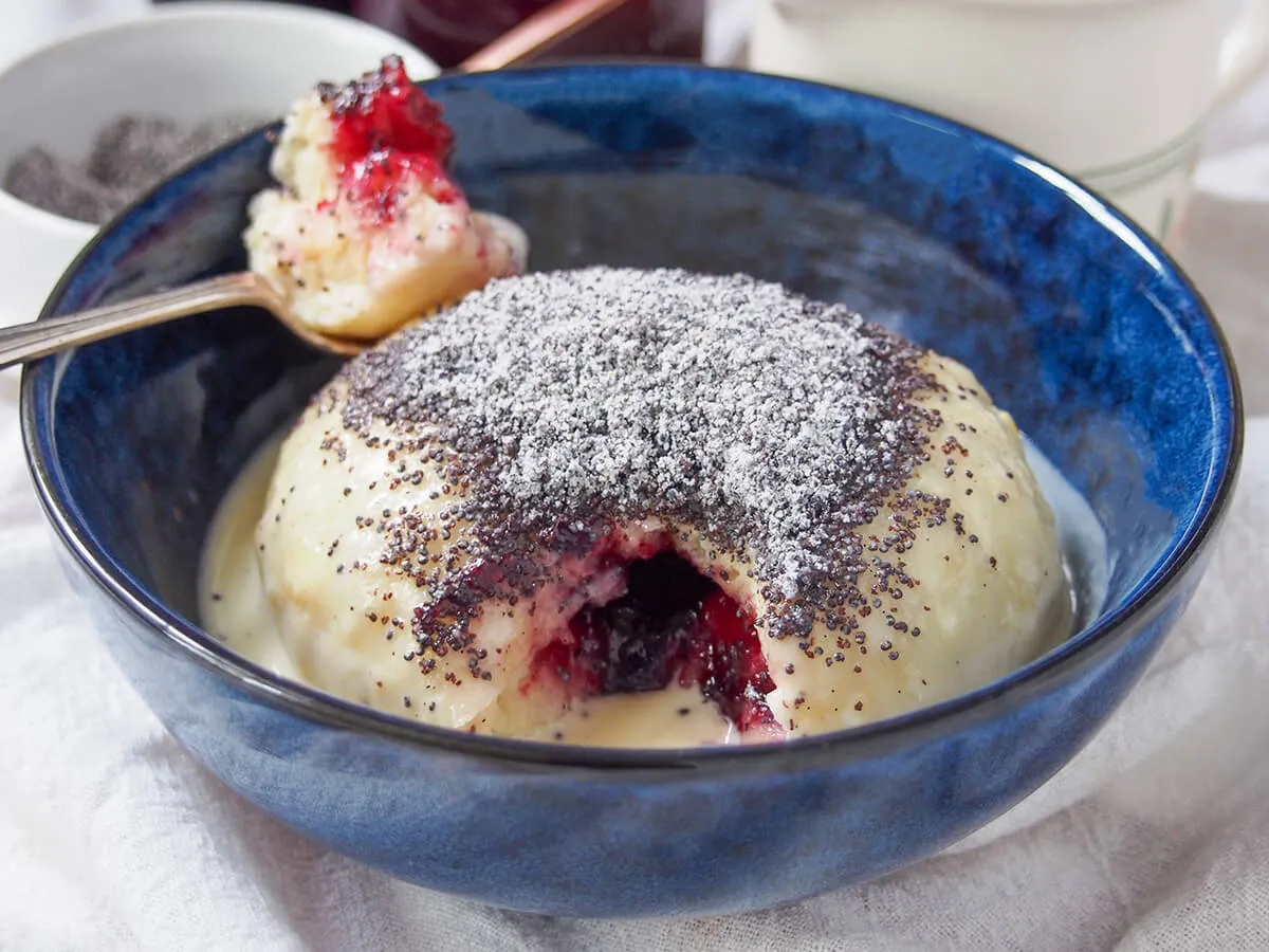 Eine Schüssel Germknödel mit einem herausgenommenen Löffel, der die Marmeladenfüllung in der Mitte zeigt.