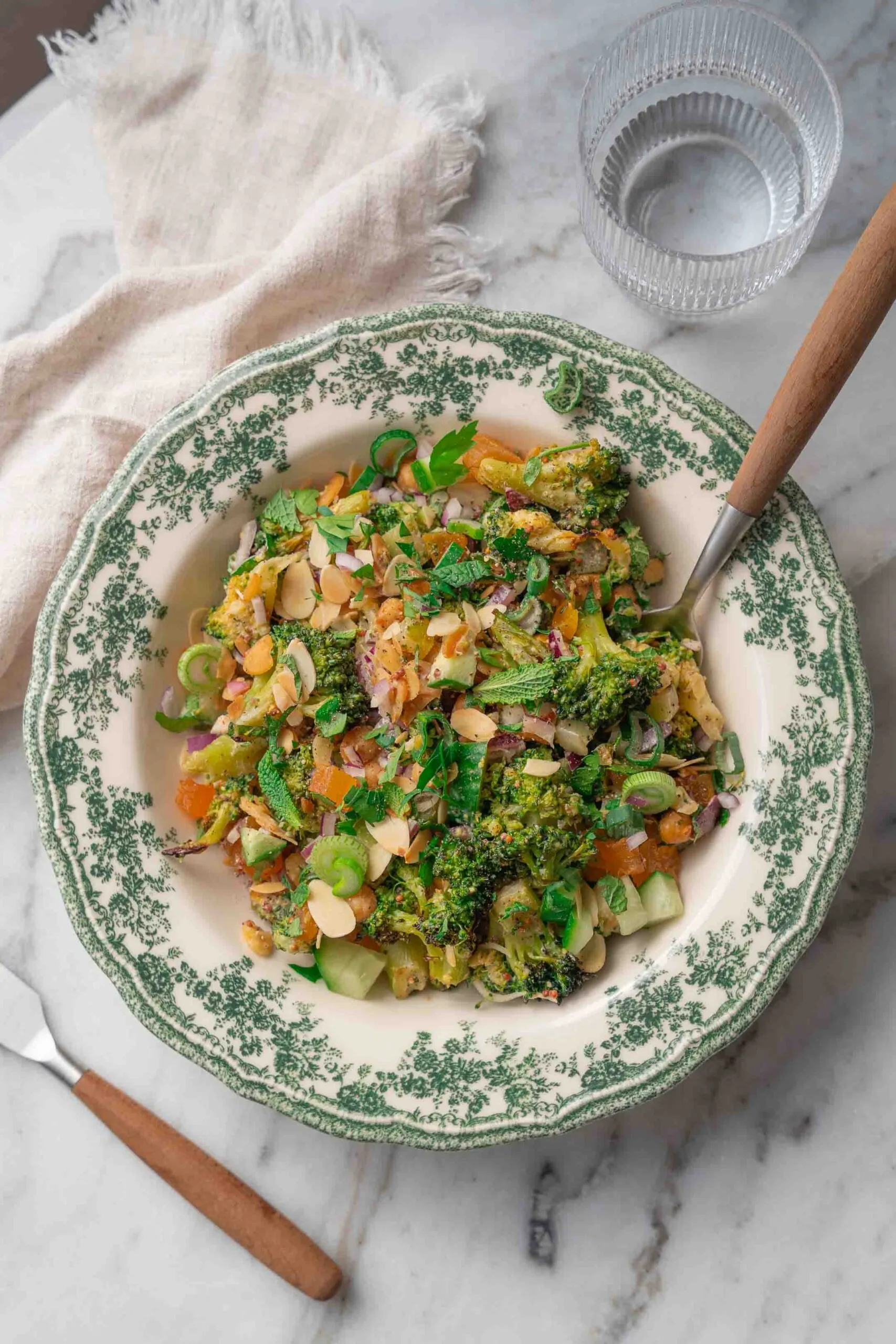 Eine Schüssel mit gemischtem Gemüsesalat mit Mandelblättchen, serviert mit einer Gabel auf einem Marmortisch.