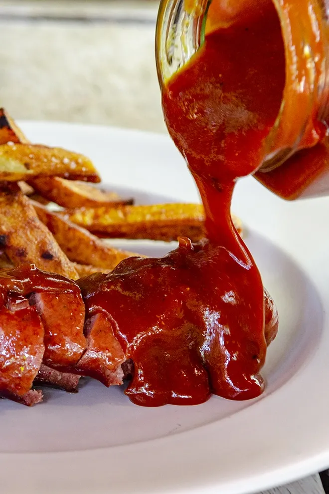 Eine Schüssel mit hausgemachter Currysauce neben einer Currywurst