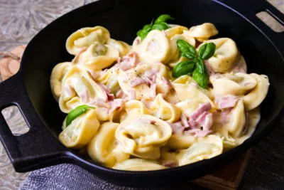 Eine Schüssel voll dampfender Tortellini alla Panna mit Schinken und Sahnesauce