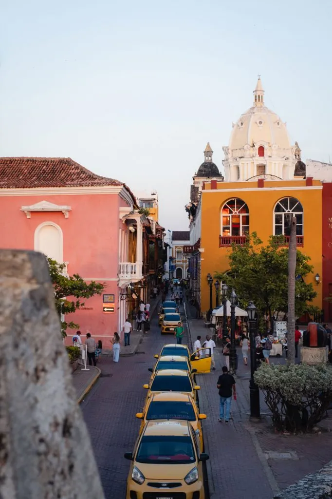 Eine Straße mit gelben Taxis, farbenfrohen Gebäuden und Menschen bei Dämmerung in einer Stadt