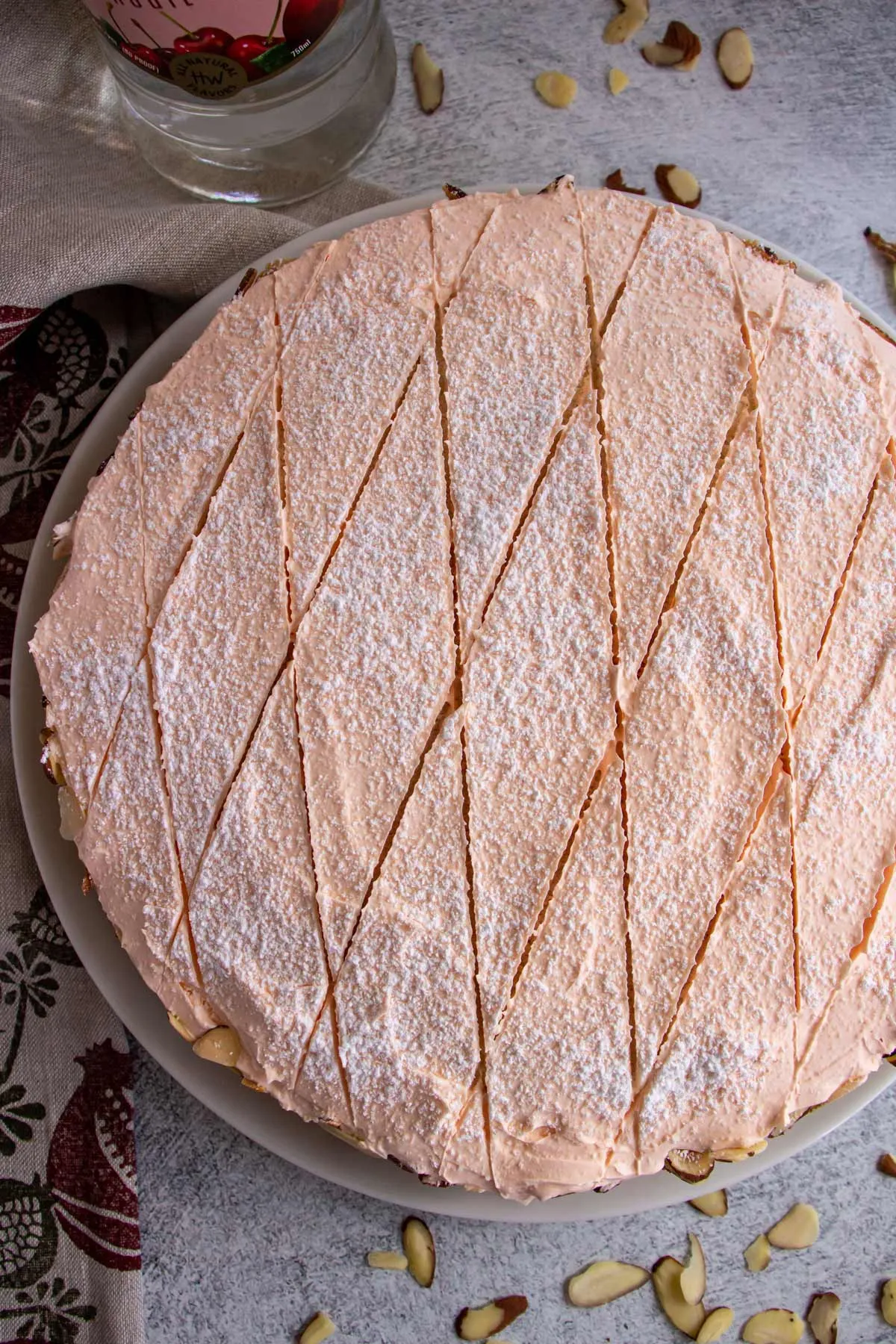 Eine Torte mit rosa Zuckerguss, Puderzucker und einem rautenförmigen Muster auf der Oberseite.