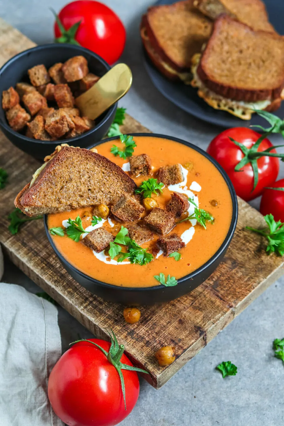 Eine vollständige Präsentation der veganen Tomatensuppe mit geröstetem Gemüse, serviert mit goldenen Croutons, Kichererbsen und einem dippbaren veganen Käse-Sandwich.
