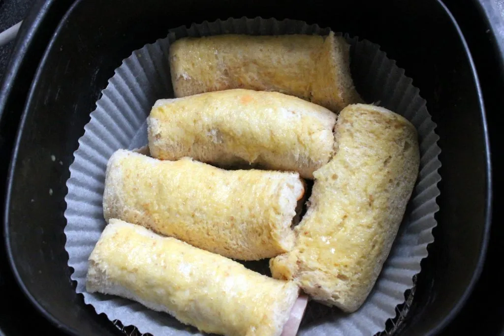 Eingepinselte Käserollen mit verquirltem Ei im Korb des Airfryers vor dem Backen