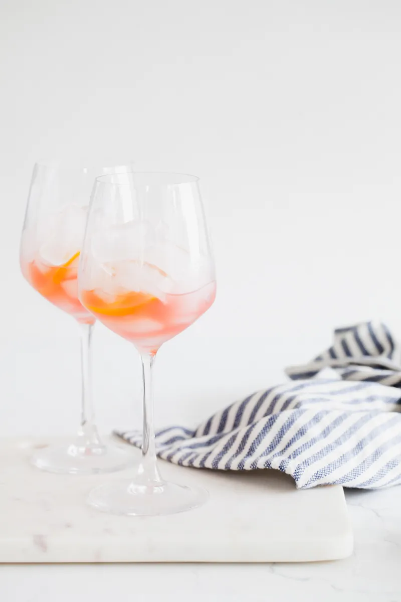 Eiswürfel und Orangenscheiben in einem Glas als Vorbereitung für den Rhabarber Aperol Spritz.