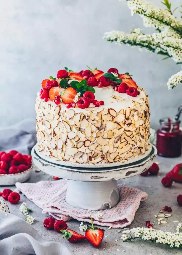 Elegante vegane Himbeer-Sahnetorte, rundherum mit Mandelblättchen verziert.