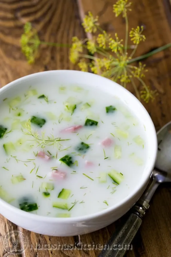 Erfrischende Okroschka-Sommersuppe in einer weißen Schale, garniert mit frischem Dill und einem Löffel daneben.