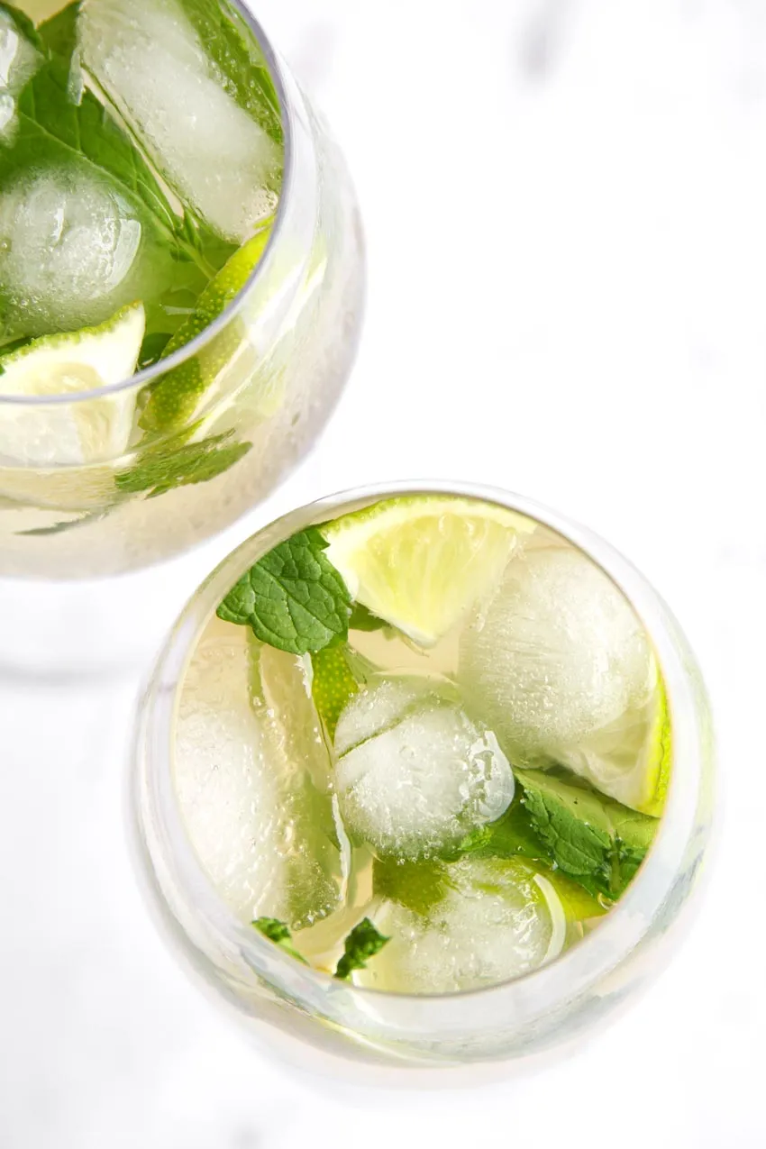 Erfrischender Hugo Spritz Cocktail mit viel Eis und frischer Minze auf einer Holzoberfläche