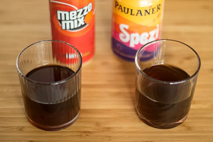 Farbvergleich von Mezzo Mix und Paulaner Spezi in Gläsern, die Nuancen des Cola-Mix-Getränks zeigend.