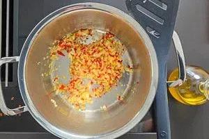 Fein gewürfelte Peperoni und Zwiebeln werden in Olivenöl in einem Topf angedünstet