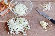 Fein gewürfelte Zwiebeln und Knoblauch auf einem Schneidebrett, vorbereitende Schritte für das Suppe kochen für Anfänger.