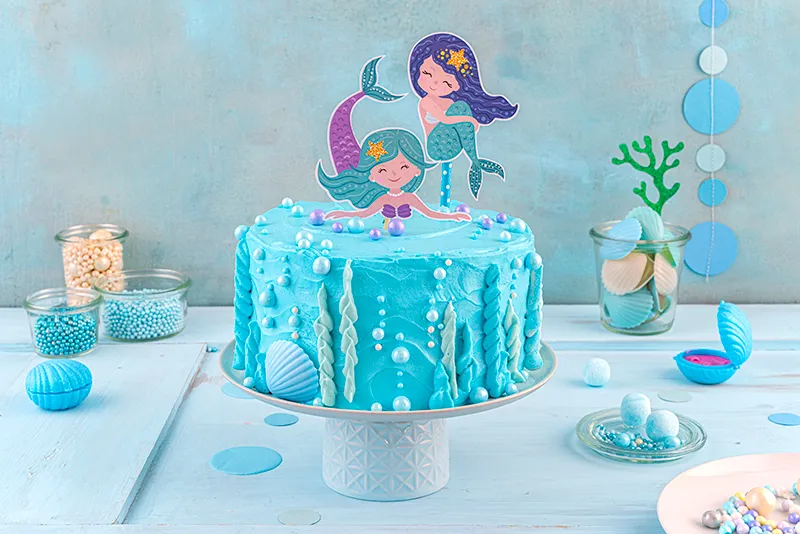 Fertig dekorierte Meerjungfrauen-Torte mit eingesteckten Mermaid-Toppern und süßen Schleckmuscheln als Akzente