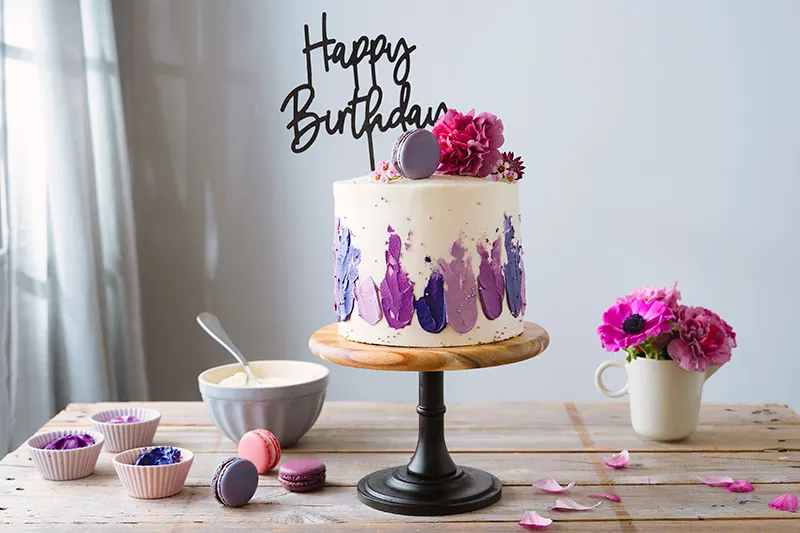 Fertig dekorierter lila Geburtstagskuchen mit Cake-Topper, Macarons und Zuckerperlen