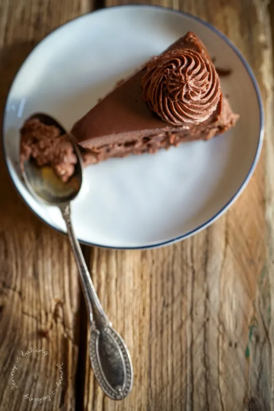 Fertig dekorierter Schokoladen-Cheesecake ohne Backen mit Sahnetupfern und Kakaopulver auf einem Holzbrett