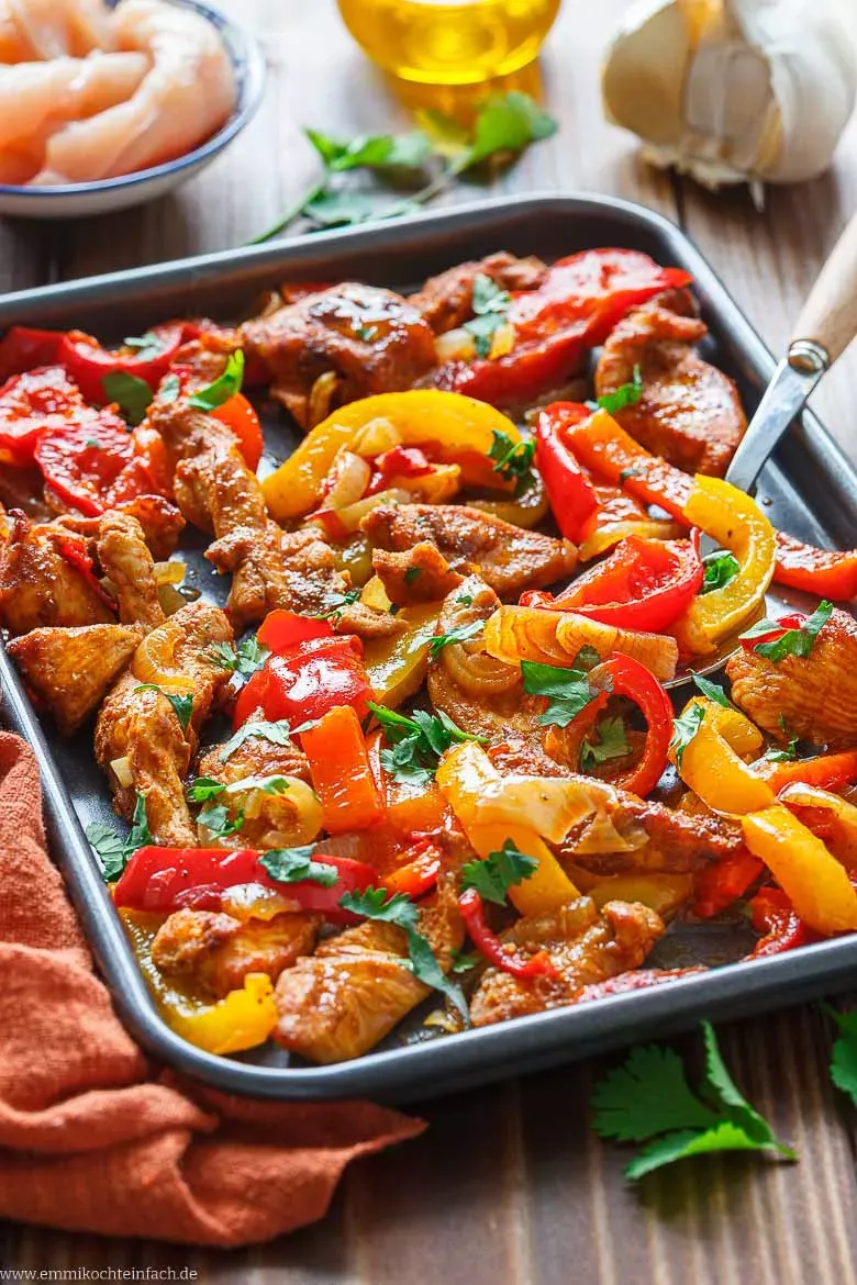 Fertig gebackene Hähnchen Fajitas vom Blech mit zarten Hähnchenstreifen, bunten Paprikas und Zwiebeln