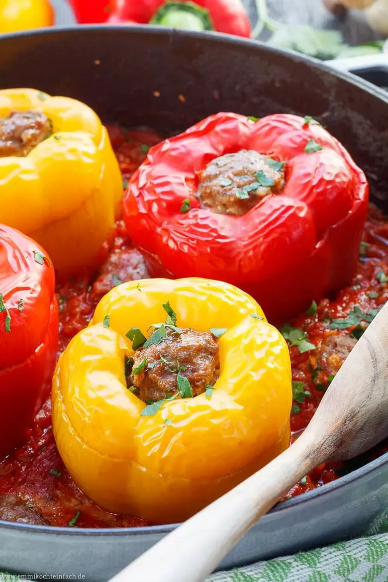 Fertig gefüllte Paprikaschoten mit Hackfleisch, umgeben von Tomatensoße im Ofentopf