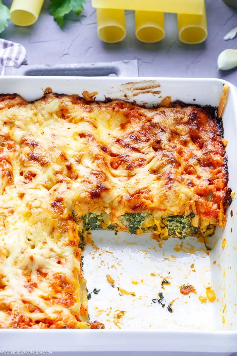 Fertig geschichtete gefüllte Cannelloni in einer Auflaufform, bedeckt mit Soße und Käse, bereit für den Backofen.