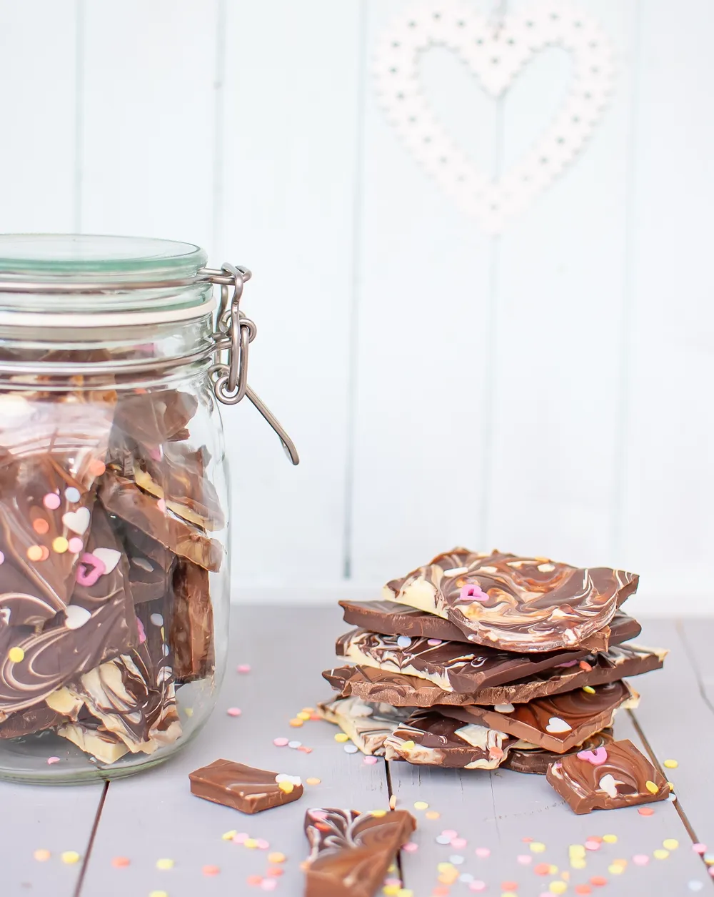 Fertige bunte Bruchschokolade mit Zuckerherzen und Konfetti auf einem Teller, perfekt als süßes Geschenk selber machen.