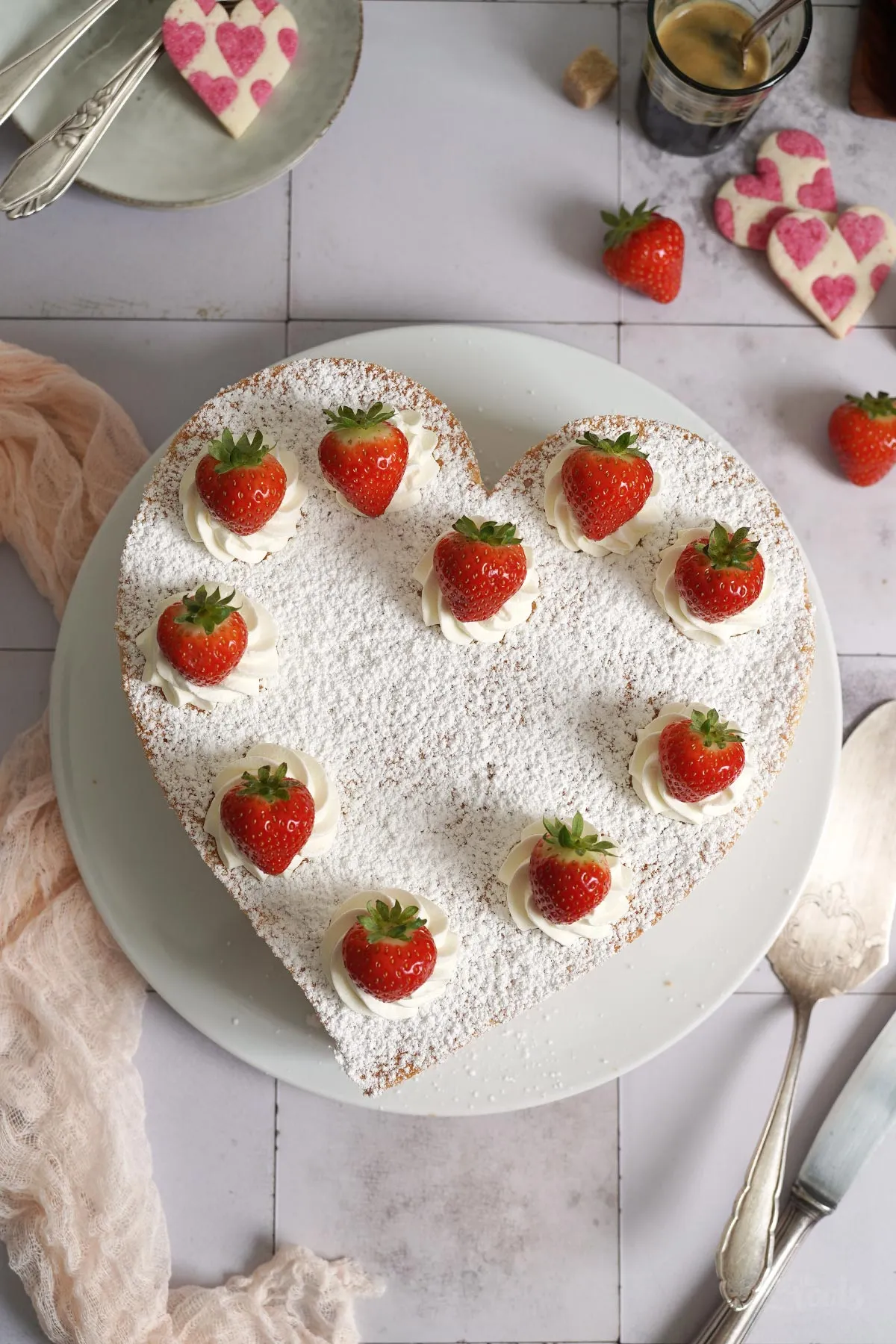 Fertige Erdbeer-Käsesahnetorte in Herzform, dekoriert mit Puderzucker und Sahnetupfen