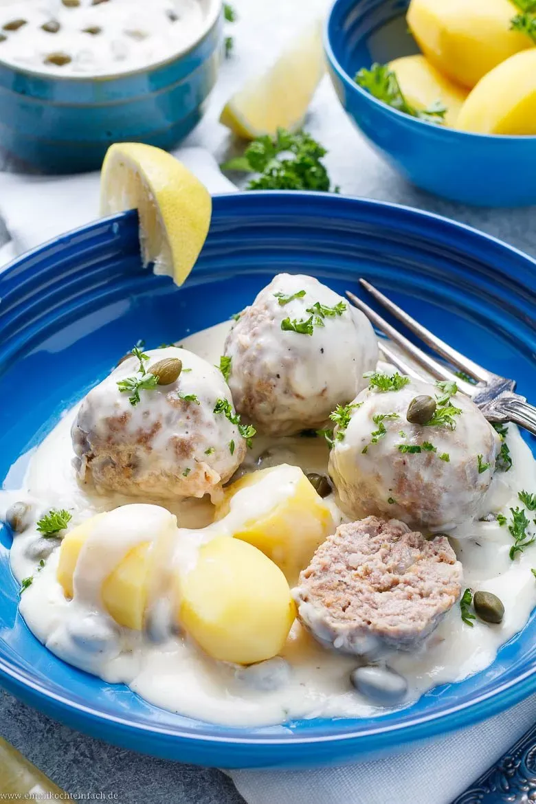 Fertige Königsberger Klopse auf einem Teller mit Salzkartoffeln und frischem Dill als Garnierung.