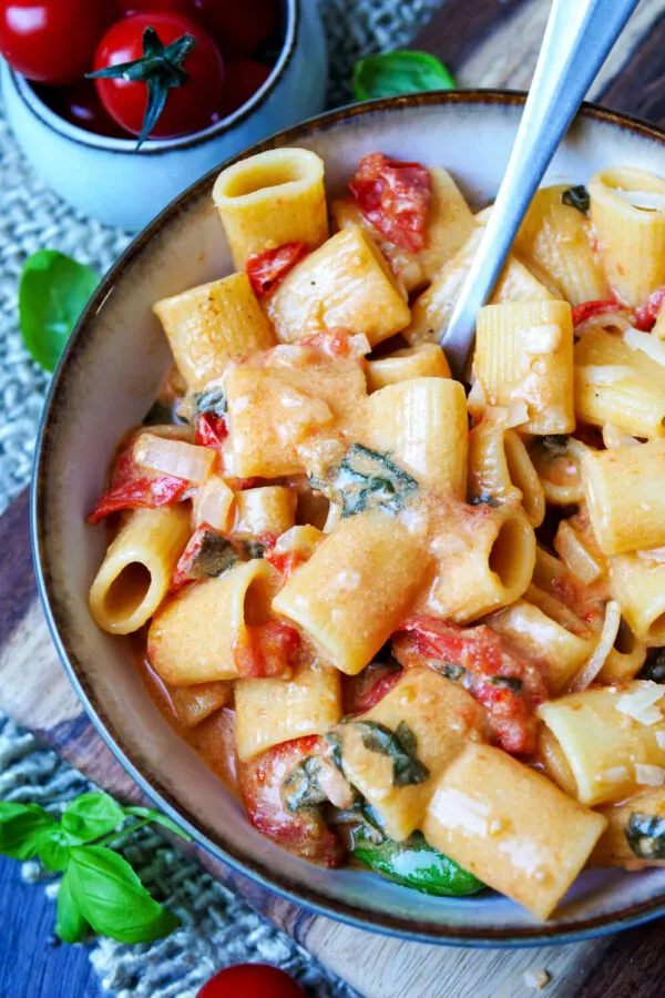 Fertige One Pot Pasta mit Kirschtomaten, frischem Basilikum und reichlich Parmesan, angerichtet auf einem Teller, perfekt als schnelles Abendessen.