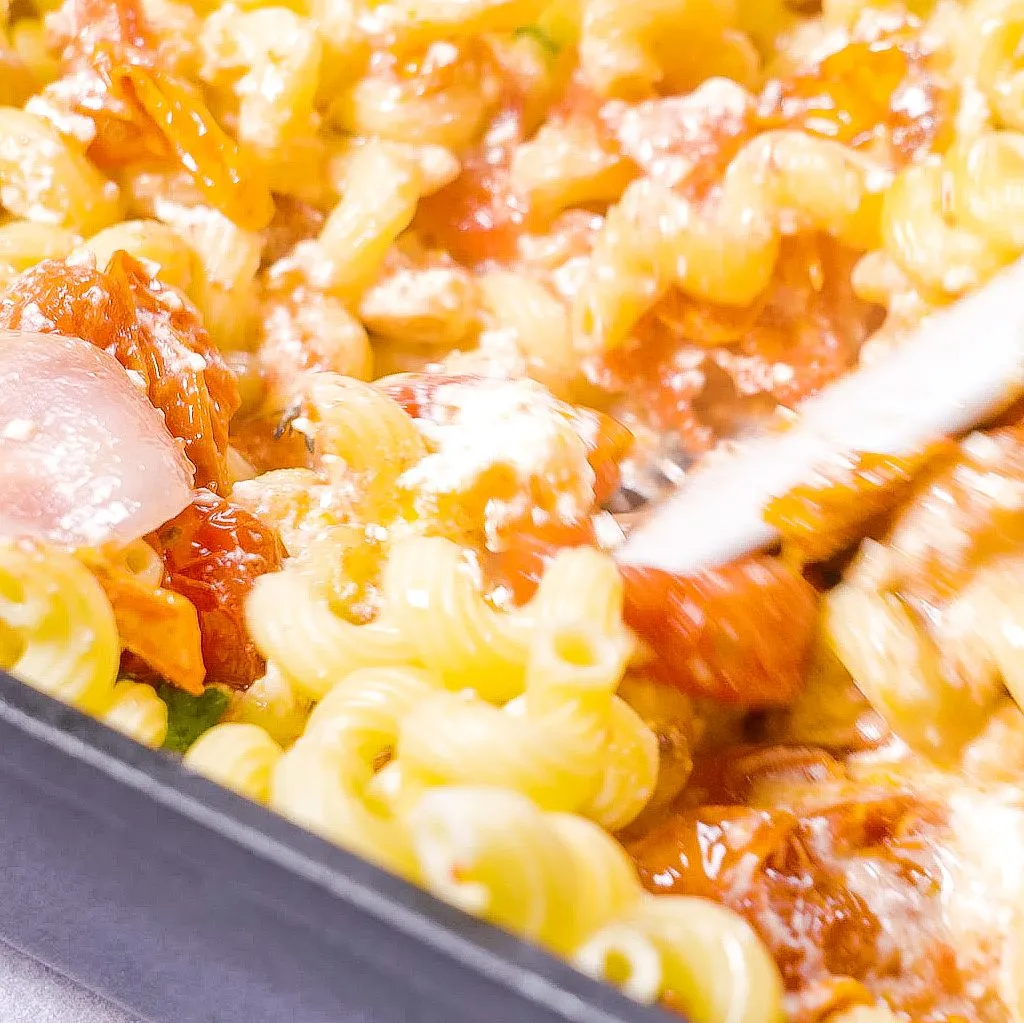 Fertige One Pot Pasta mit Schafskäse und Tomaten, vermischt in der Auflaufform, garniert mit frischem Basilikum und servierbereit.