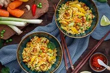 Fertiger gebratener Reis mit Ei, Gemüse und Hähnchen, garniert mit Koriander und Limettenspalte, bereit zum Servieren