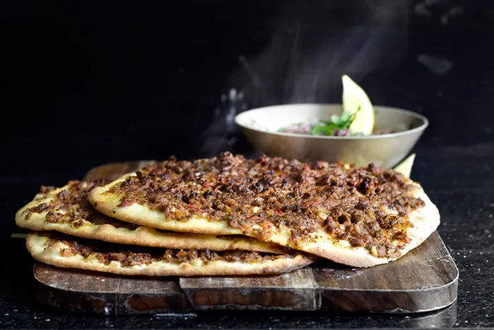 Fertiges Lahmacun auf einem Schneidebrett mit Salat und Zitrone