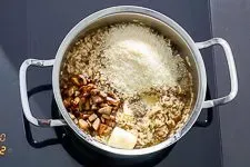 Fertiges Pilzrisotto wird mit Parmesan und gebratenen Pilzen verfeinert.
