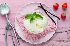 Fertiges selbstgemachtes Vanilleeis wird mit einem Eislöffel aus dem gekühlten Behälter geschöpft