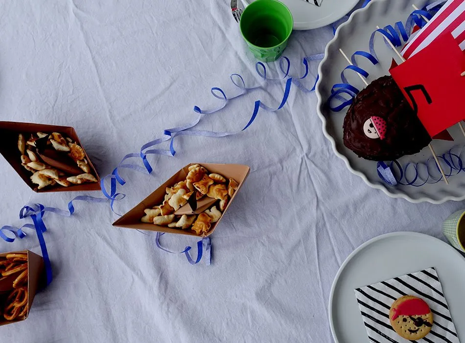 Festlich gedeckter Geburtstagstisch mit einem kunstvollen Piratenschiff-Kuchen aus Schokolade und Snacks.